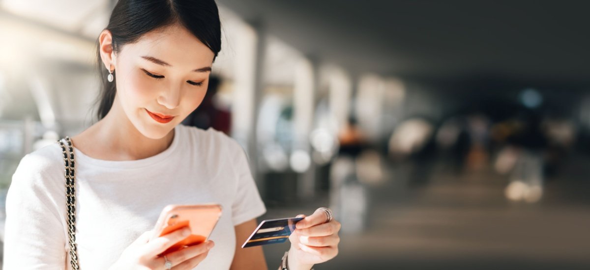 young-woman-holding-credit-card-checking-phone-at-airport